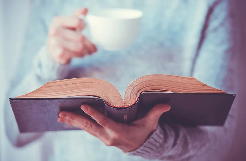 Persona leyendo un libro con una taza en la mano